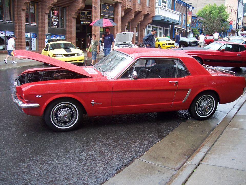 Red classic Ford Mustang coupe, side view, hood up, at a wet-street car show