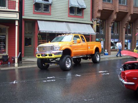 Lifted orange Ford pickup with flames and big tires on a wet street
