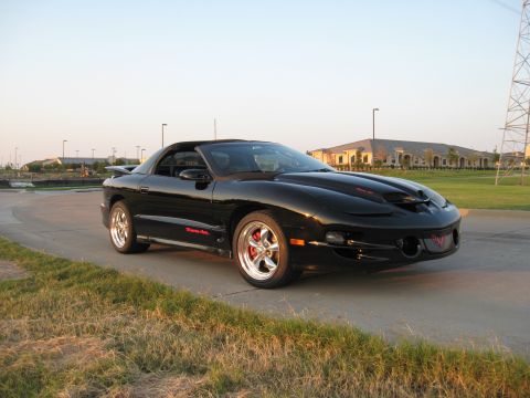 2002 Pontiac Trans Am - A black Pontiac Trans Am is parked on a paved surface with grass and buildings in the background.