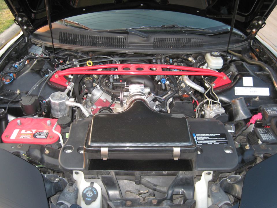 Engine bay of a car with a red strut bar, black air intake cover, and red battery