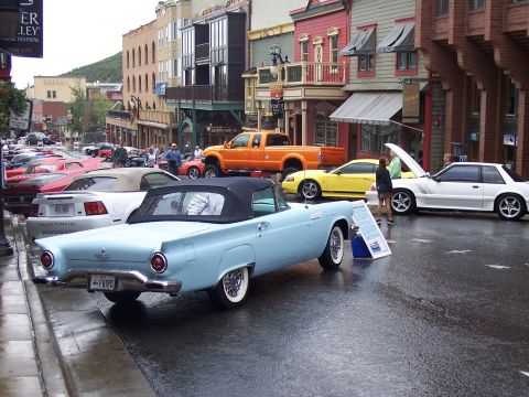 1972 Ford Ranchero - Light blue 1957 Ford Thunderbird convertible parked on a wet street during a car show.