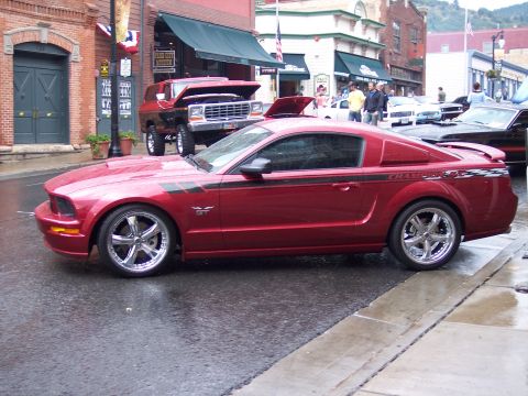 1972 Ford Ranchero - A red Ford Mustang GT coupe is parked on a wet street next to other vehicles.