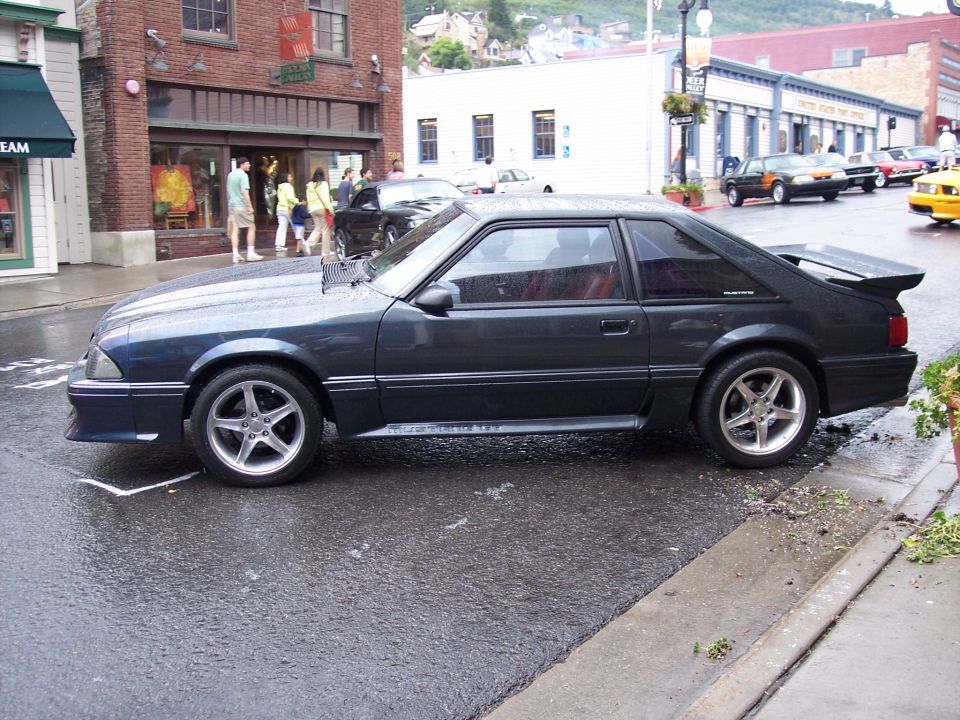 Dark gray coupe with a spoiler parked on a wet street, side view