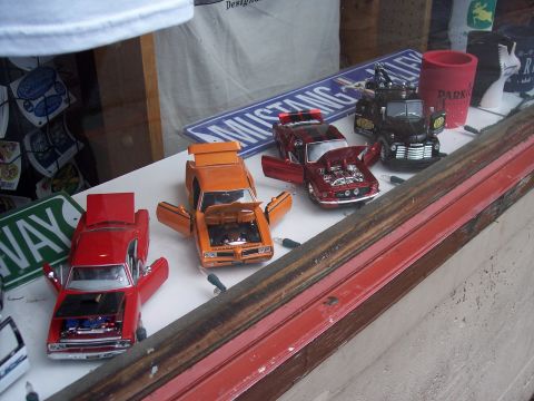 1972 Ford Ranchero - A collection of model cars, including a red, an orange, and a dark red vehicle, are displayed with various signs and decorations.