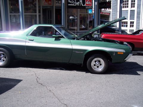 1972 Ford Ranchero - A green pickup truck is parked on a street with its hood up, next to a red pickup truck.