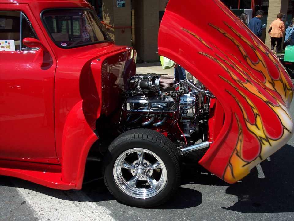 Red hot rod with custom flame paint on the hood and a chrome engine exposed. Chrome five-spoke wheels are visible