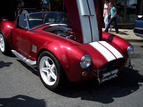 1972 Ford Ranchero - A red convertible sports car with white racing stripes is parked on a street with its hood open.