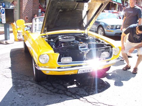 1972 Ford Ranchero - A bright yellow convertible with its hood open is displayed, with a modern blue car visible in the background.