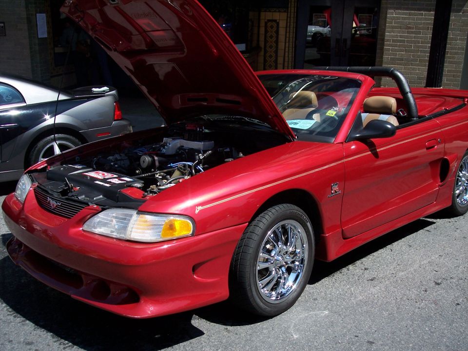 Red convertible Mustang with hood open, showing engine. Chrome wheels