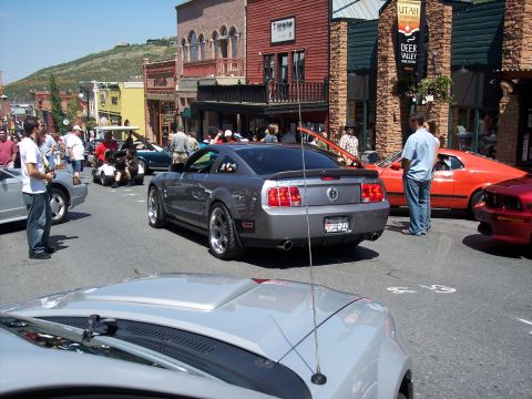 1972 Ford Ranchero - A gray Ford Mustang is parked on a street with other cars and people.