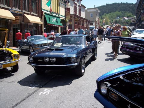 1972 Ford Ranchero - A dark blue classic coupe is parked on a street lined with buildings and people.