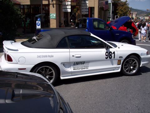 1972 Ford Ranchero - A white convertible with racing decals is parked on a street next to other vehicles.