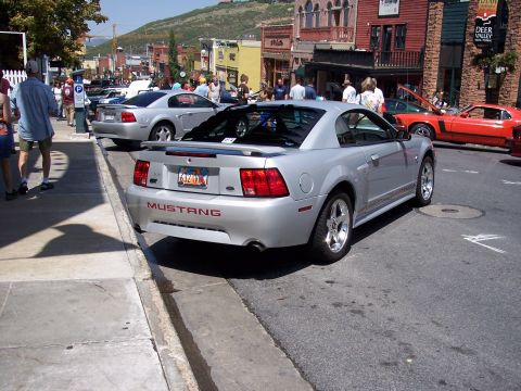 1972 Ford Ranchero - A silver Ford Mustang convertible is parked on a street with other vehicles and pedestrians.