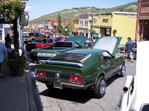 1972 Ford Ranchero - A green muscle car is parked on a street with other vehicles and buildings in the background.