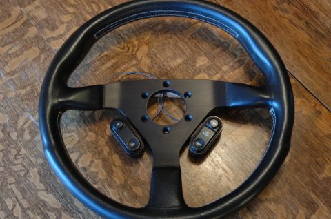 1984 Ford Bronco - A black steering wheel with cruise control buttons is shown against a wooden background.
