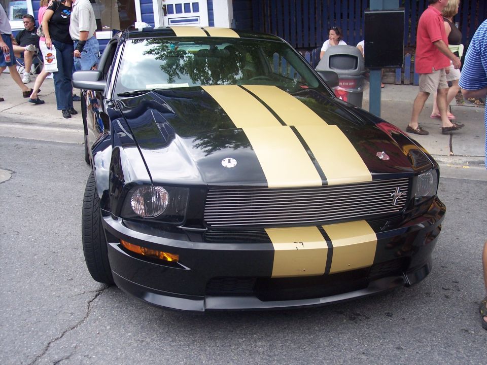 Black Ford Mustang with gold racing stripes, front view