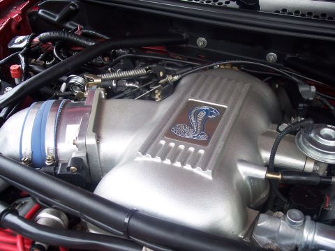 1972 Ford Ranchero - Close-up of an engine intake manifold a Cobra emblem, with visible hoses and wiring.