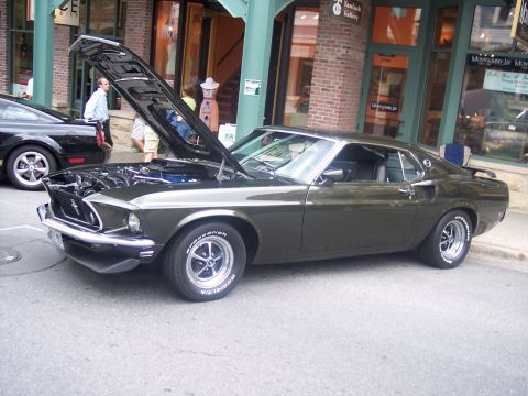 1972 Ford Ranchero - A classic Ford Mustang is displayed with its hood up on a street in front of shops.