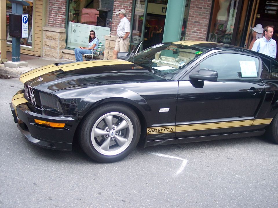 Black Ford Mustang Shelby GT-H with gold stripes, front passenger side view, parked on asphalt