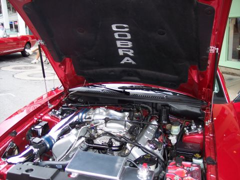 1972 Ford Ranchero - The "Cobra" emblem is visible on the hood liner of this red vehicle's engine bay, with another classic red car in the background.