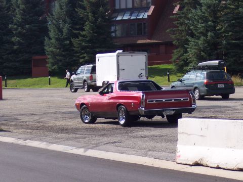1972 Ford Ranchero - A red 1970 Ford Ranchero is parked in a lot with other vehicles and a building in the background.