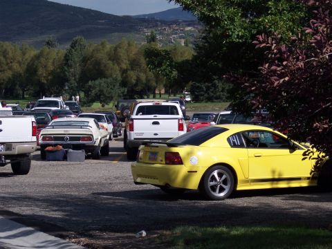 1972 Ford Ranchero - A bright yellow coupe with racing numbers is parked in a lot, with other vehicles and trees in the background.