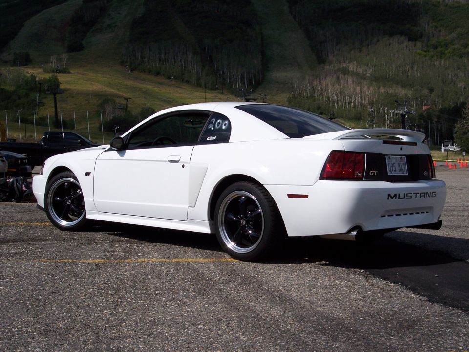 White Ford Mustang GT parked on asphalt with a ski slope in the background. Number 200 is on the side window
