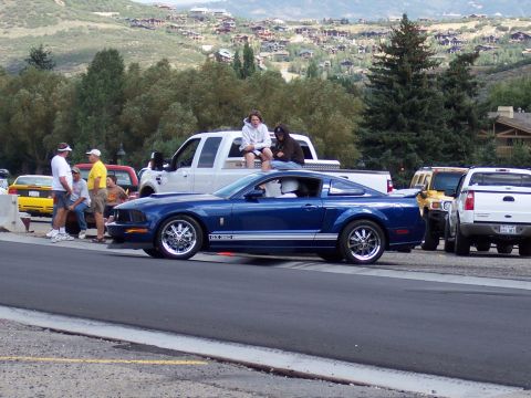 1972 Ford Ranchero - A blue Ford Mustang GT is parked on the side of the road with other vehicles and people in the background.
