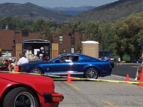 1972 Ford Ranchero - A blue Ford Mustang is parked in front of a trailer, with a red car in the foreground and mountains behind.