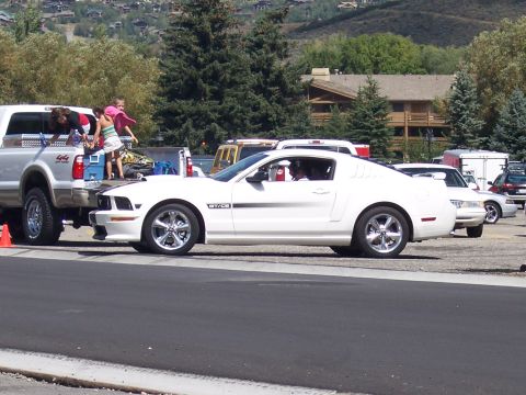 1972 Ford Ranchero - A white Ford Mustang GT/CS is parked next to a silver pickup truck with people loading items into the truck bed.