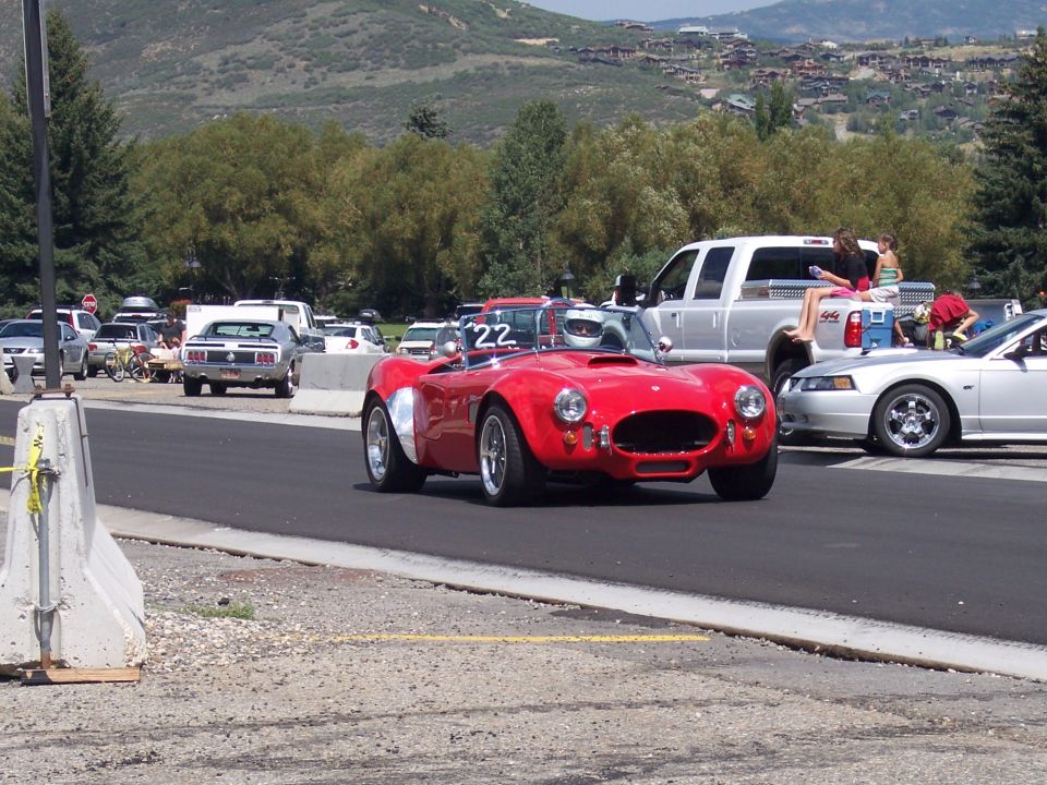 Red convertible sports car with racing number 22 on windshield, parked near a silver pickup truck and a silver Mustang