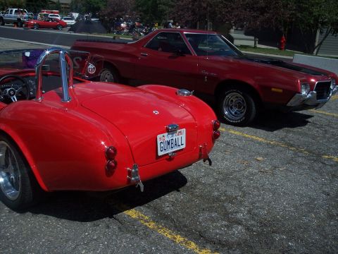 1972 Ford Ranchero - A red 1972 Ford Ranchero is parked next to a red convertible. The Ranchero has a black stripe on its hood.
