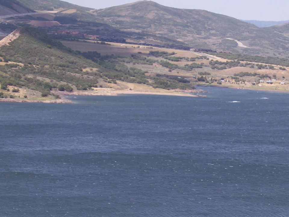 Wide shot of a large body of water with hills and a road in the background