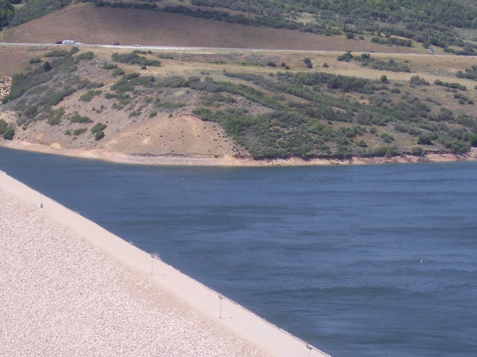 Vehicles on a distant highway above a body of water and a dam