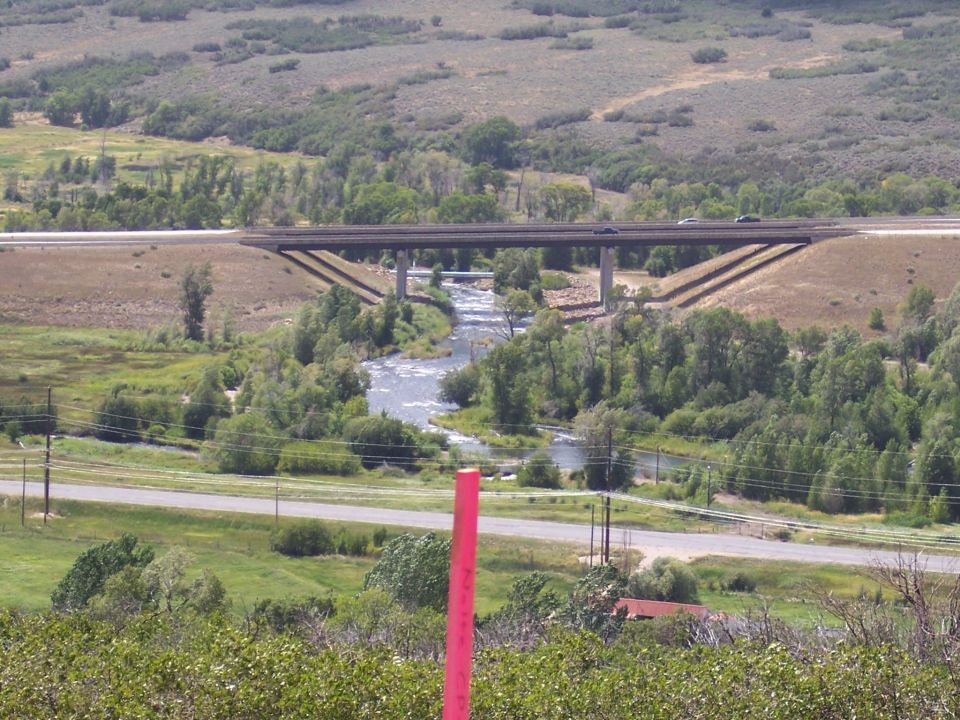 Two cars on a highway overpass above a river and trees