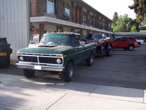 1972 Ford Ranchero - A green Ford pickup truck tows a red car on a trailer in front of a motel.