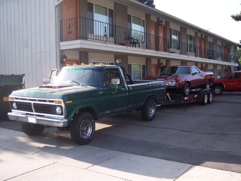 1972 Ford Ranchero - A green 1975 Ford pickup truck tows a red car on a trailer in front of a motel.