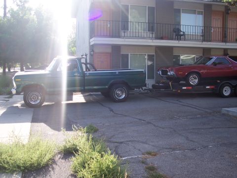 1972 Ford Ranchero - A red 1972 Ford Ranchero is seen on a trailer being towed by a green pickup truck.