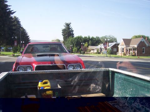 1972 Ford Ranchero - A red coupe with a prominent hood scoop is parked on a street, viewed from the back of a pickup truck.