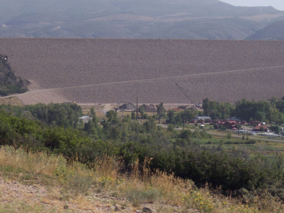 Large dam wall with distant buildings and trees in the foreground