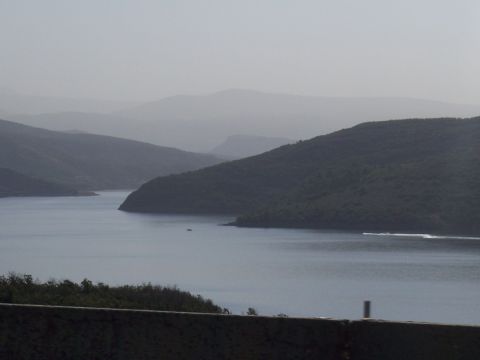 1972 Ford Ranchero - A wide shot of a hazy mountain range surrounding a calm body of water, with a small boat visible in the distance.