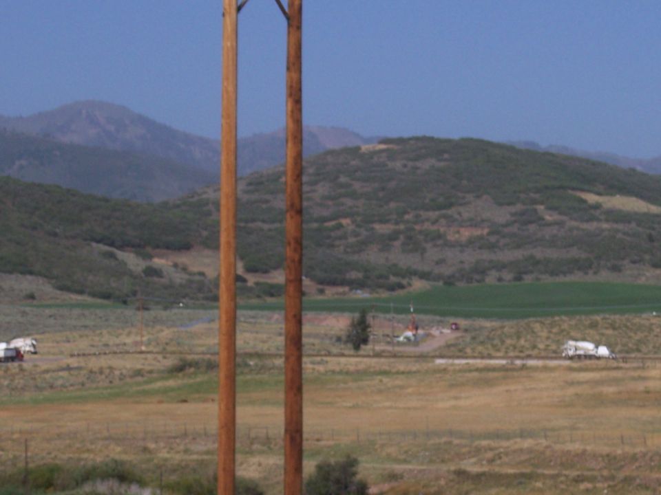 Two trucks drive on a road in a rural landscape with hills and power poles