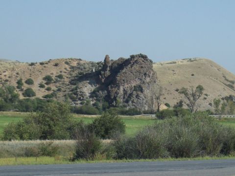 1972 Ford Ranchero - A prominent rock formation stands tall against a backdrop of arid hills and green fields under a clear sky.