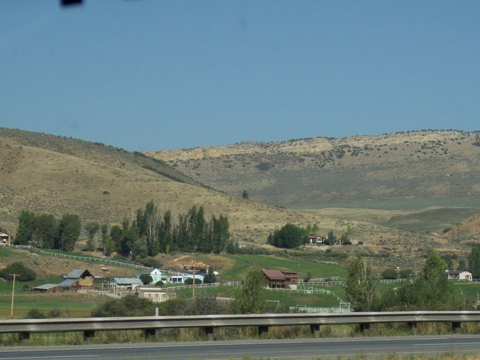 Rural landscape with rolling hills and scattered farm buildings under a clear blue sky