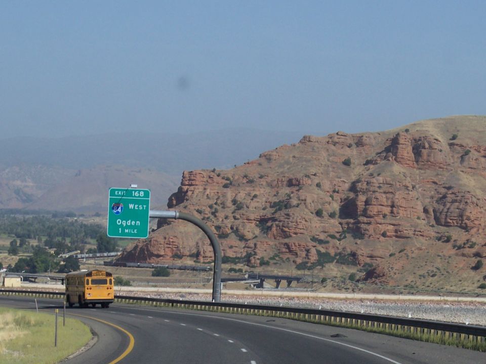 Yellow school bus on highway with red rock formations and Ogden exit sign