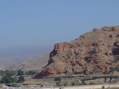1972 Ford Ranchero - A train travels along tracks at the base of a large, red, rocky hill under a clear blue sky.