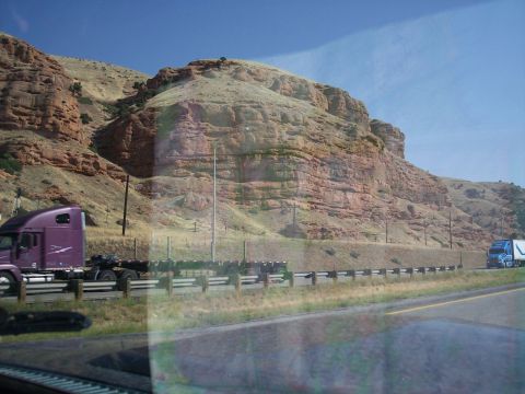 1972 Ford Ranchero - Two semi-trucks travel along a highway with a backdrop of , layered rock formations under a clear blue sky.