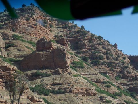 1972 Ford Ranchero - A view of a rocky hillside with scattered trees and bushes under a bright blue sky.