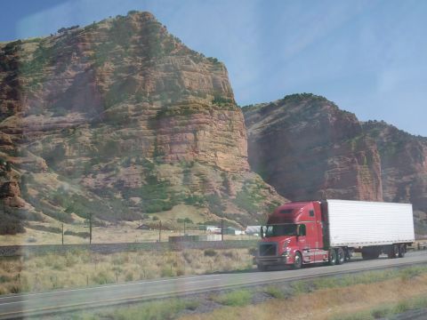 1972 Ford Ranchero - A red semi-truck travels down a highway with large, layered rock formations in the background under a clear blue sky.