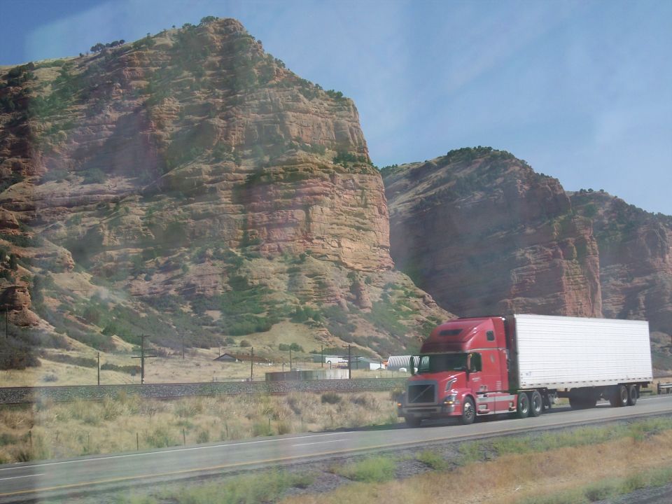 Red semi-truck drives on a highway past rocky mountains